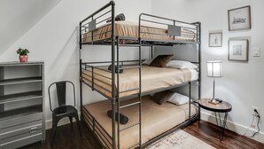 Ein Etagenbett mit Schreibtisch und Stuhl, ein kleiner Tisch mit Lampe sowie gerahmte Bilder an der Wand.