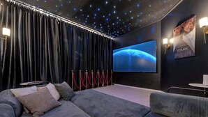 A cinema room with a large screen, dark curtains, red stanchions, and a sofa. - 5-bd/2.5-ba With Pool, Hot Tub, Cinema & Golf Sim (Royse City)