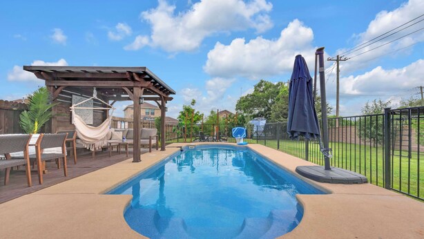 A rectangular swimming pool with a 3 ft depth marker, surrounded by a deck with chairs and a covered seating area. - 5-bd/2.5-ba With Pool, Hot Tub, Cinema & Golf Sim (Royse City)