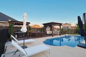 A backyard with a swimming pool, lounge chairs, a barbecue area, and a pergola. - 5-bd/2.5-ba With Pool, Hot Tub, Cinema & Golf Sim (Royse City)