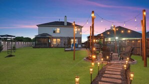 A backyard with a stone pathway, outdoor seating, and string lights. - 5-bd/2.5-ba With Pool, Hot Tub, Cinema & Golf Sim (Royse City)