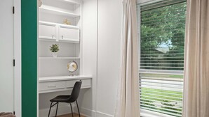 Ein Zimmer mit Schreibtisch, Stuhl, Regalen und einem Fenster mit Jalousien.