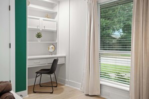 Ein Zimmer mit Schreibtisch, Stuhl, Regalen und einem Fenster mit Jalousien.