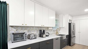 Eine moderne Küche mit weißen Schränken, einem Edelstahlkühlschrank, einem Toaster und einer Kaffeemaschine.