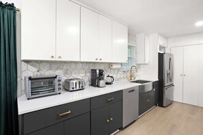 Eine moderne Küche mit weißen Schränken, einem Edelstahlkühlschrank, einem Toaster und einer Kaffeemaschine.