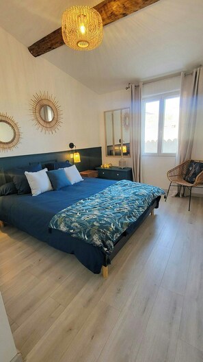 A bedroom with a large bed, a wooden ceiling beam, a hanging light fixture, and a chair. - Artist's house between sea and vineyards (Florensac)