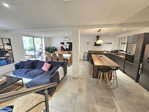 A modern living room with a sofa, a dining area with a wooden table and chairs, and a kitchen with a bar area. - Artist's house between sea and vineyards (Florensac)
