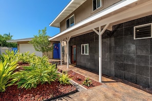 Ein zweistöckiges Haus mit überdachter Veranda, Garage und einem angelegten Vorgarten mit Pflanzen und Kies.