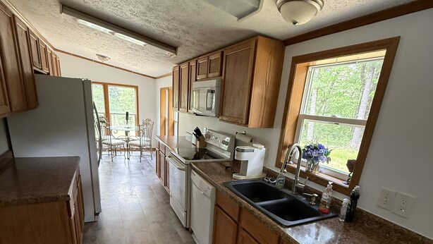 A kitchen with wooden cabinets, a stainless steel refrigerator, a dishwasher, a sink, and a window with a view of greenery. -  Four Bedroom Woodland Retreat Near Downtown Wisconsin Dells! (Wisconsin Dells)
