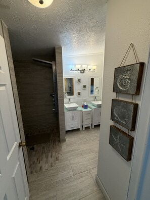 A bathroom with a shower, a vanity with a sink, and a mirror. There are wall-mounted lights above the vanity.