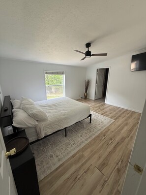A bedroom with a bed, a ceiling fan, a window, and a door.