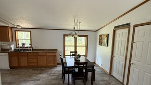 A spacious kitchen with wooden cabinets, a dining table with chairs, a chandelier, and a large window. -  Four Bedroom Woodland Retreat Near Downtown Wisconsin Dells! (Wisconsin Dells)