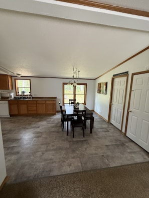A spacious kitchen with wooden cabinets, a dining table with chairs, a chandelier, and a large window.