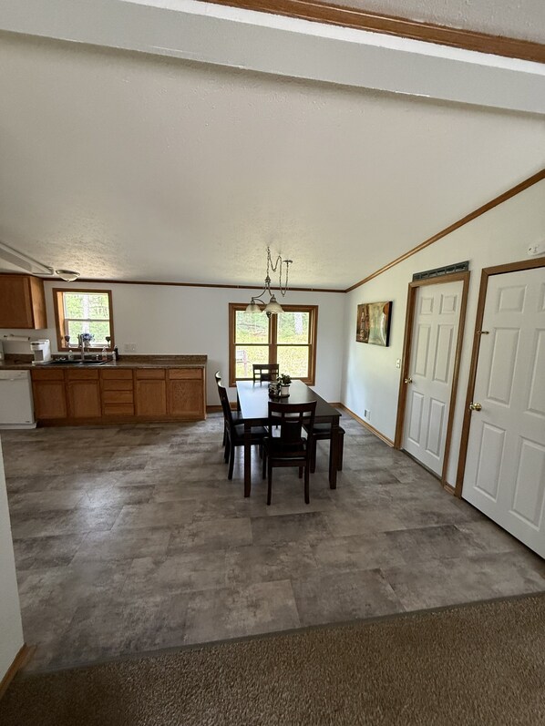 A spacious kitchen with wooden cabinets, a dining table with chairs, a chandelier, and a large window.
