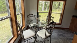 A dining area with a glass table and metal chairs, large windows with a view of trees, and a ceiling with a light fixture. -  Four Bedroom Woodland Retreat Near Downtown Wisconsin Dells! (Wisconsin Dells)