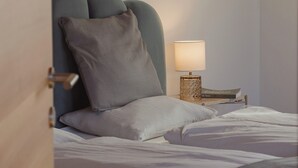 Een net opgemaakt bed met kussens, een bedlampje en een nachtkastje met boeken.