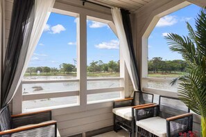 A covered outdoor seating area with wicker chairs and a view of a water body and park. - Luxury Condo, Waterviews, Pools, 12PM Check In (Myrtle Beach)