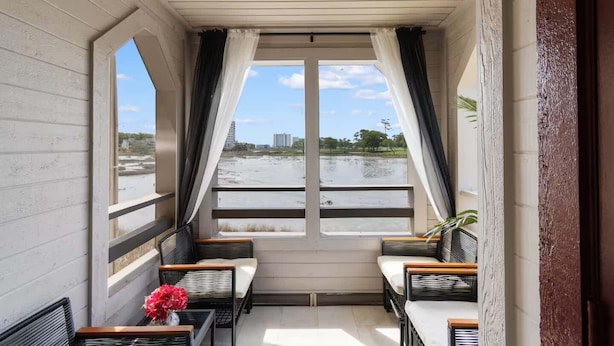 Ein Balkon mit Korbmöbeln, einem Blumentopf und Blick auf ein Gewässer und Gebäude.