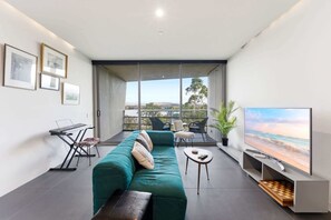 Ein modernes Wohnzimmer mit einem türkisfarbenen Sofa, einem Klavier, einem Flachbildfernseher und einem Balkon mit Blick.