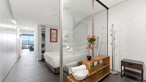 A modern bedroom with a bed, a wooden nightstand, a mirror, and a view of a balcony. - Lake View 1-Bed Apartment Canberra Centre (Canberra)