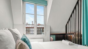 A bedroom with a large window, a bed with white linens, and a view of a building outside. - Suite elegante entre Tour Eiffel et Invalides (Paris)