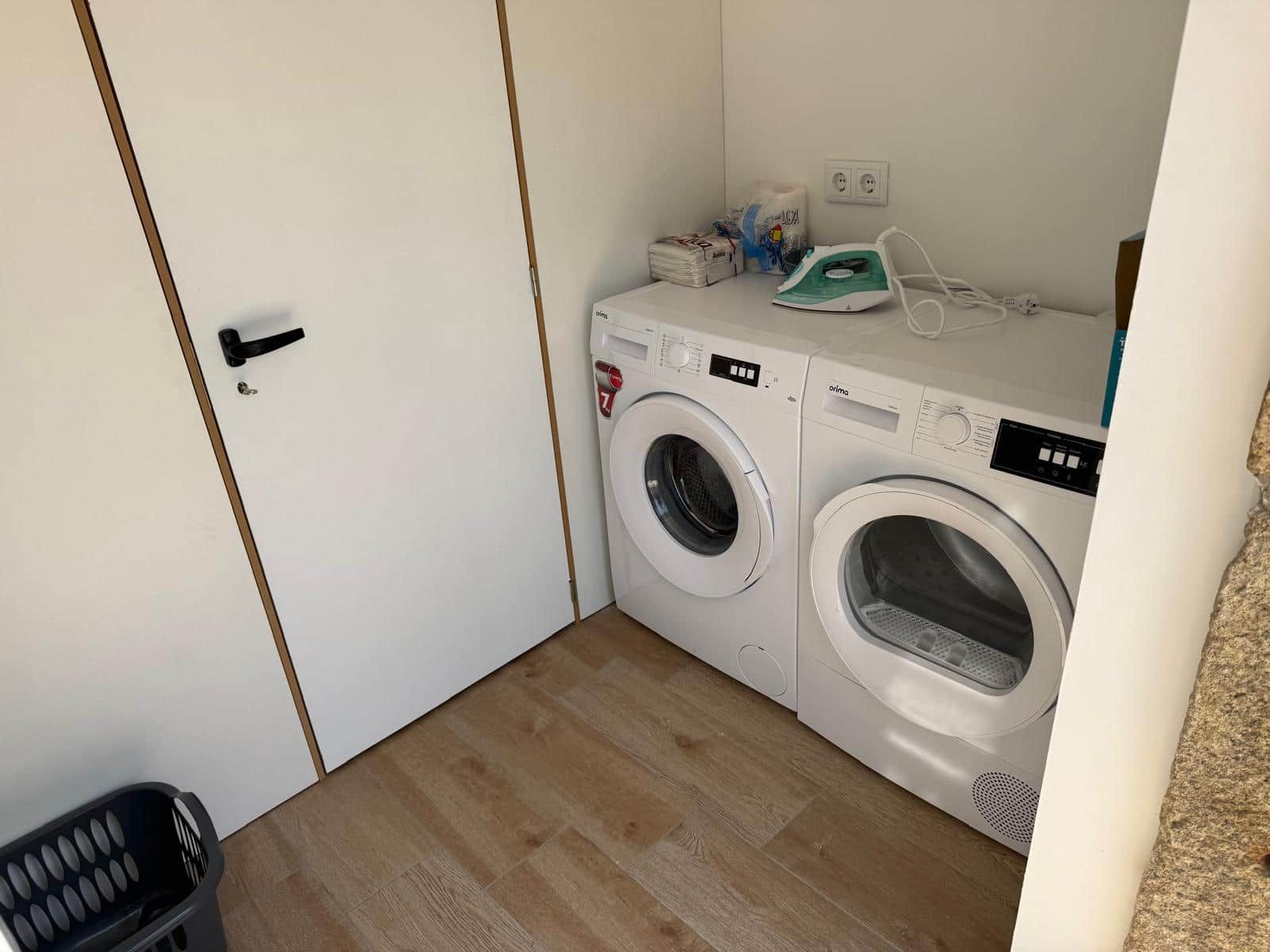 A compact laundry area with a washing machine and dryer, a basket, and a door.