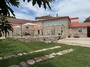 A stone building with a red-tiled roof, a stone patio with a wooden bench, and a grassy lawn.