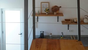 Ein Zimmer mit schrägverdeckter Decke, Holzbalken, einer Pendelleuchte, einem Holztisch und einer Küchenzeile mit Spüle und Arbeitsplatte.