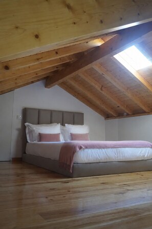 A bedroom with a sloped ceiling, wooden beams, a bed with white and pink bedding, and a skylight.
