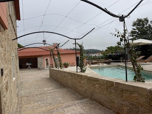 A stone-walled pool area with a tiled patio, a red-roofed building, and a hanging light fixture.