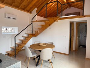 A wooden staircase leading to a loft bedroom, a dining area with a round table and chairs, and a shower room.