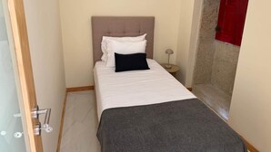 Un dormitorio pequeño y ordenado, con cama, lámpara de noche y una puerta roja.