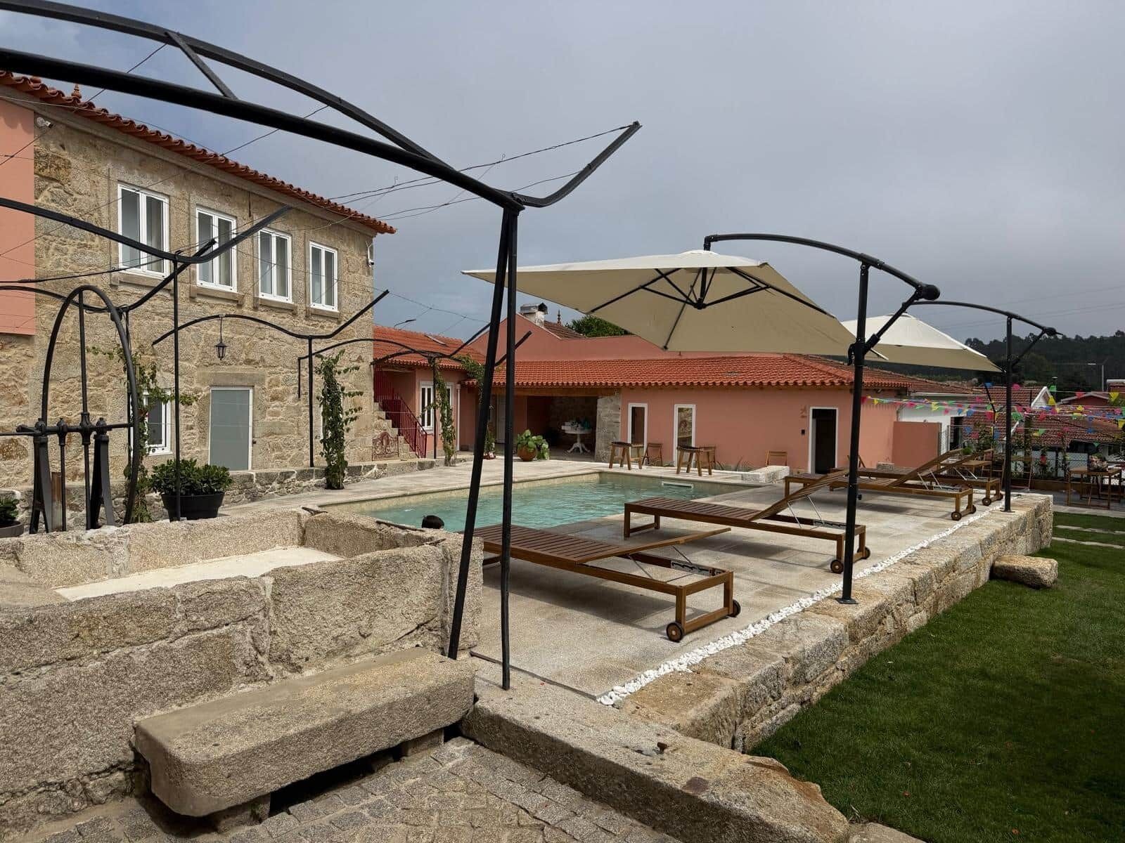 Un área de piscina con sillones de descanso, un edificio de piedra y una construcción con techo rojo.