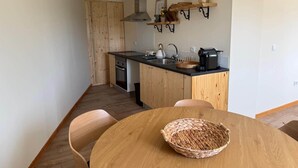 Eine kompakte Küche mit Holdekor-Schränken, einer schwarzen Arbeitsplatte, einem Herd und einem Spülbecken. Ein Esstisch mit Stühlen und einem gewebten Korb stehen bereit.