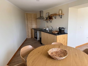 A compact kitchen with wooden cabinets, a black countertop, a stove, and a sink. There is a dining table with chairs and a woven basket on it. - Family-friendly apartment with a pool on the Camino de Santiago (Macieira da Maia)