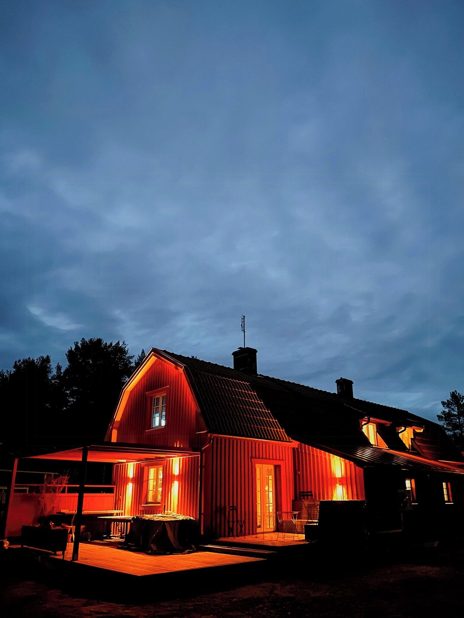 En rød, lade-lignende bygning med skrå tag, synlig skorsten og en lille veranda.