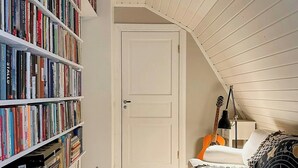Une pièce avec un plafond en pente, une bibliothèque remplie de livres, un lit avec une literie à motifs et une guitare.