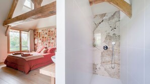 A bedroom with a large bed, a wooden ceiling, and a bathroom with a shower.