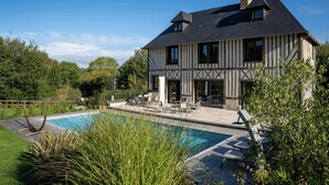A two-story house with a swimming pool, outdoor furniture, and a garden.