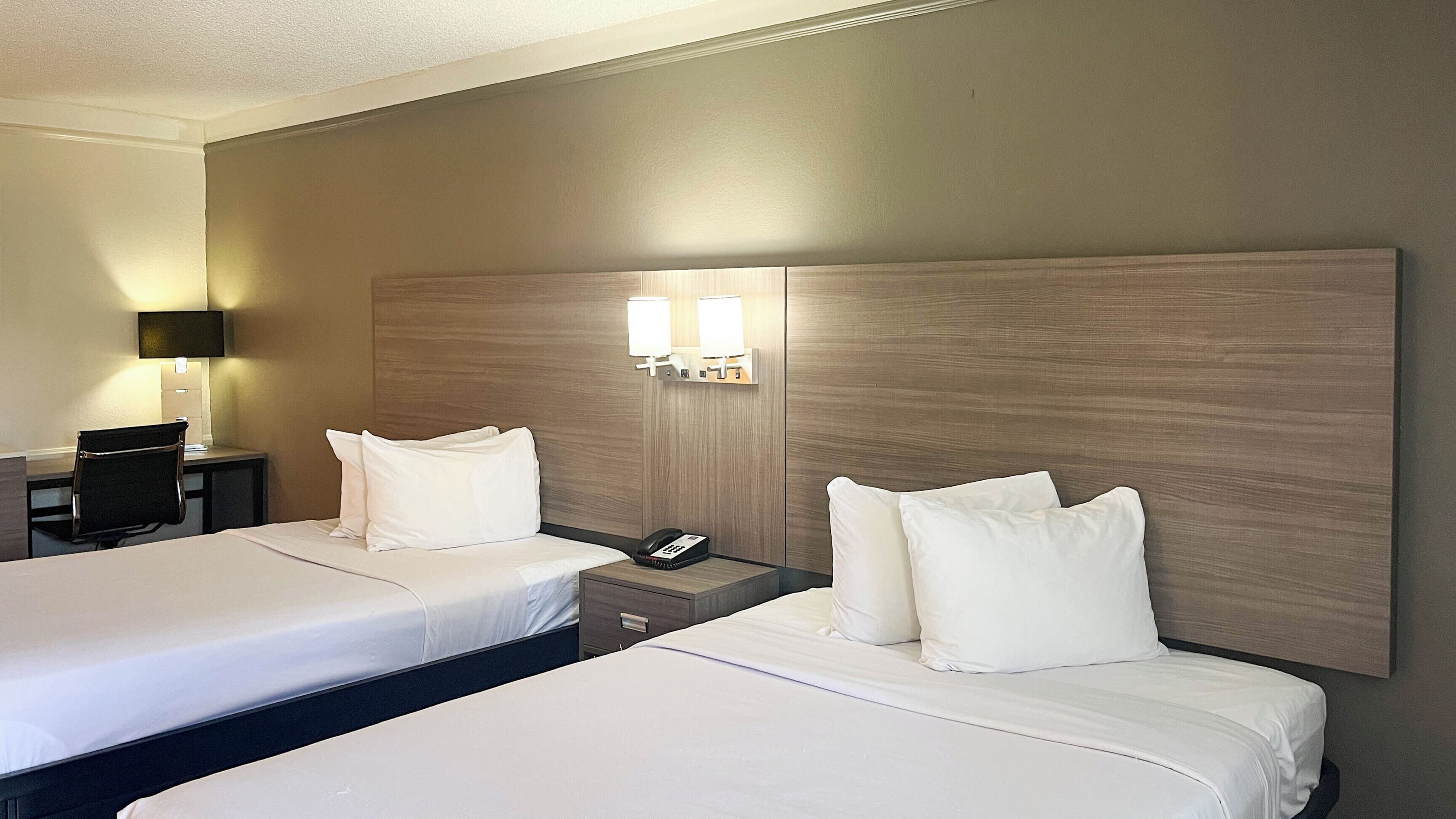 Een hotelkamer met twee bedden, een bureau, een stoel, een lamp en een telefoon op het nachtkastje.