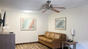Una habitación con ventilador de techo, un sofá de cuero marrón, una mesita con un teléfono y dos cuadros abstractos enmarcados en las paredes.