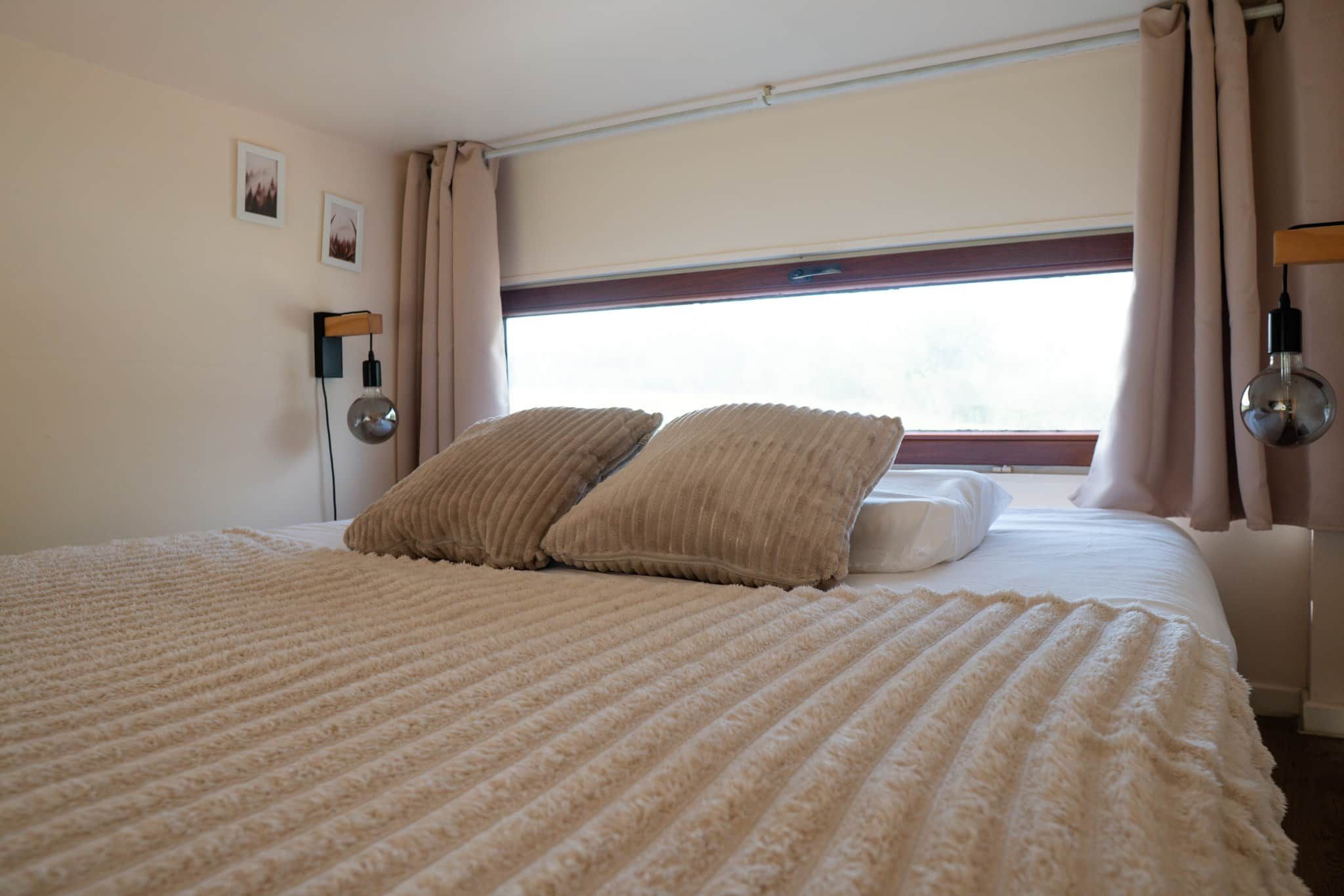 Une chambre d’hôtel avec un grand lit, deux oreillers, une fenêtre avec des rideaux et une lampe fixée au mur.