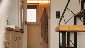 A hallway with a wooden floor, a staircase with a geometric design, a coat hanging on the wall, and a door leading to another room. - Maple Cottage - Tiny House with private spa (Profondeville)