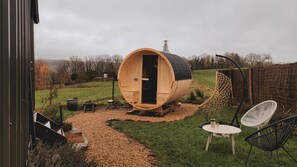 A wooden sauna structure with a door, a hanging chair, and a table with a bottle. - Maple Cottage - Tiny House with private spa (Profondeville)