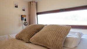 Un llit amb dos almoiners, una làmpada de nit i una finestra amb cortines.