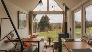 A modern kitchen with a large window, a dining area with a table and chairs, and a staircase. - Maple Cottage - Tiny House with private spa (Profondeville)
