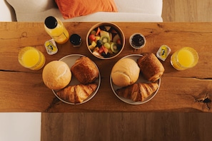 Una mesa de madera con alimentos para el desayuno, como cruasanes, fruta y jugo.