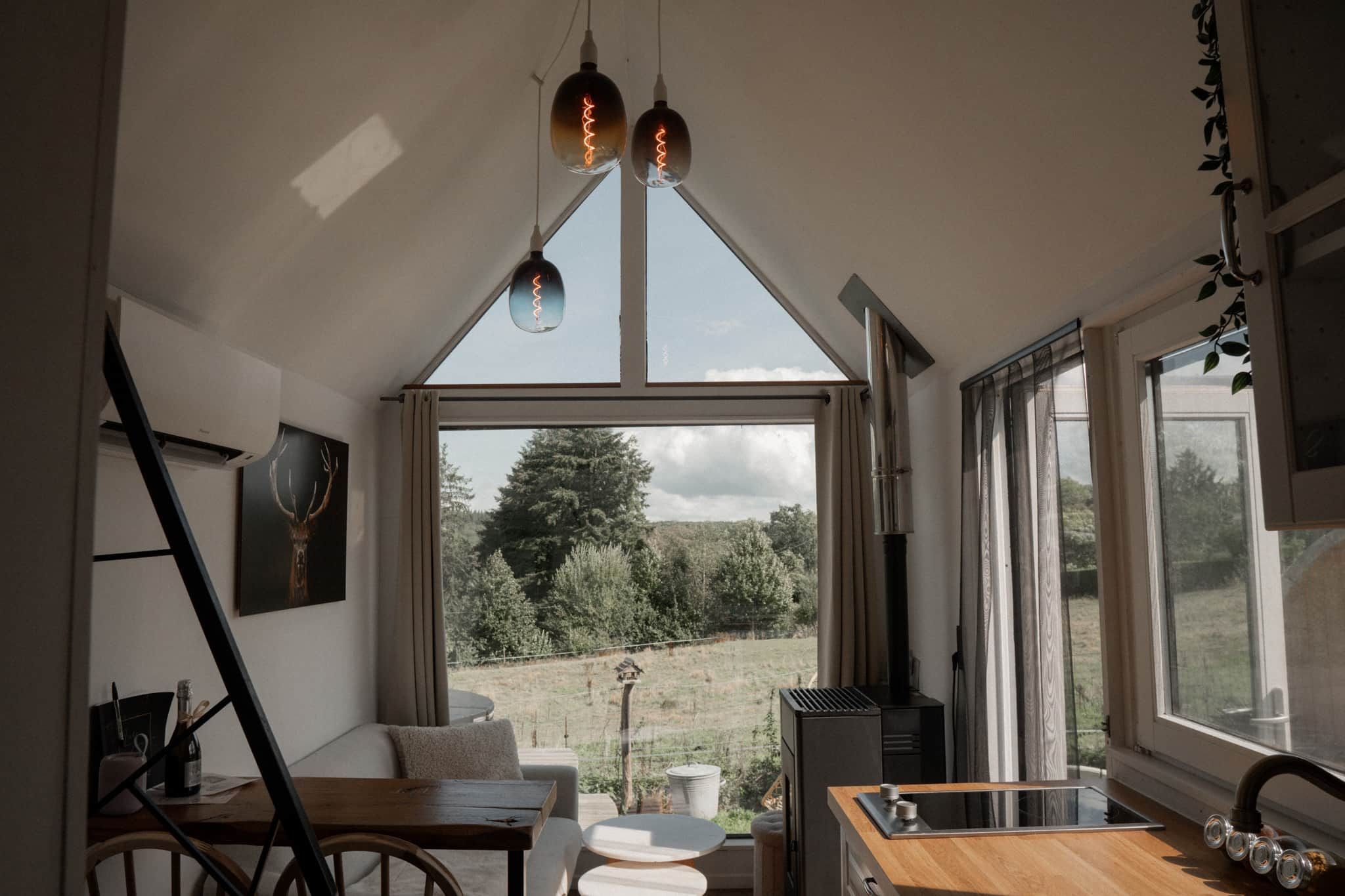 Eine moderne Küche mit einem großen Fenster, einem Essbereich mit Tisch und Stühlen und Blick auf eine grüne Landschaft.