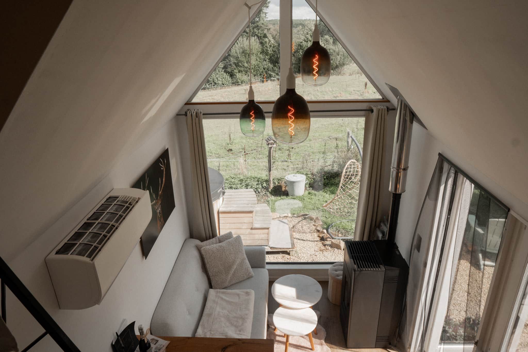 Habitación espaciosa con techo alto, unidad de aire acondicionado integrada, sofá, una mesita y vista a un jardín a través de un ventanal grande.