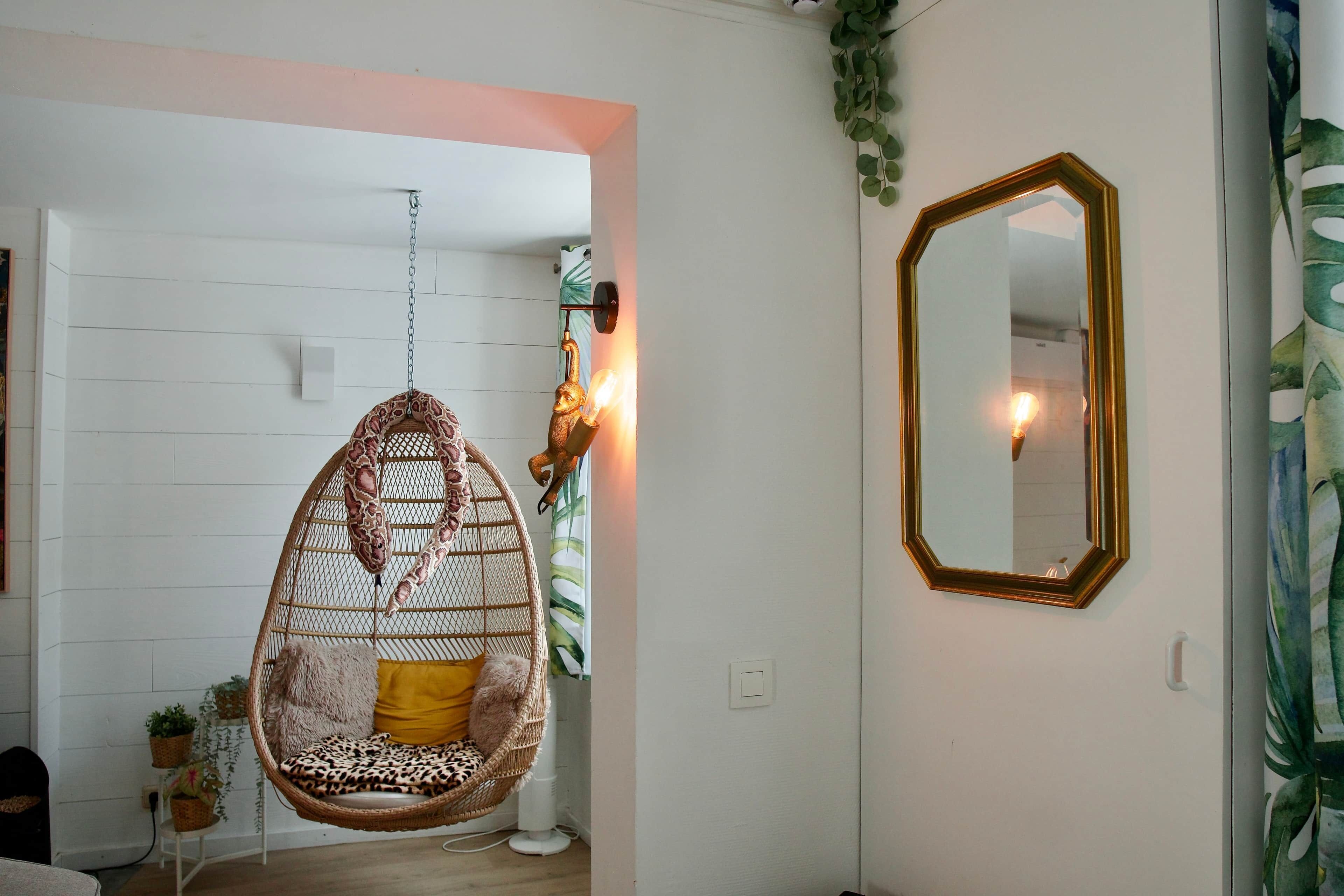 Une pièce avec un fauteuil suspendu, un miroir et un luminaire fixé au mur.